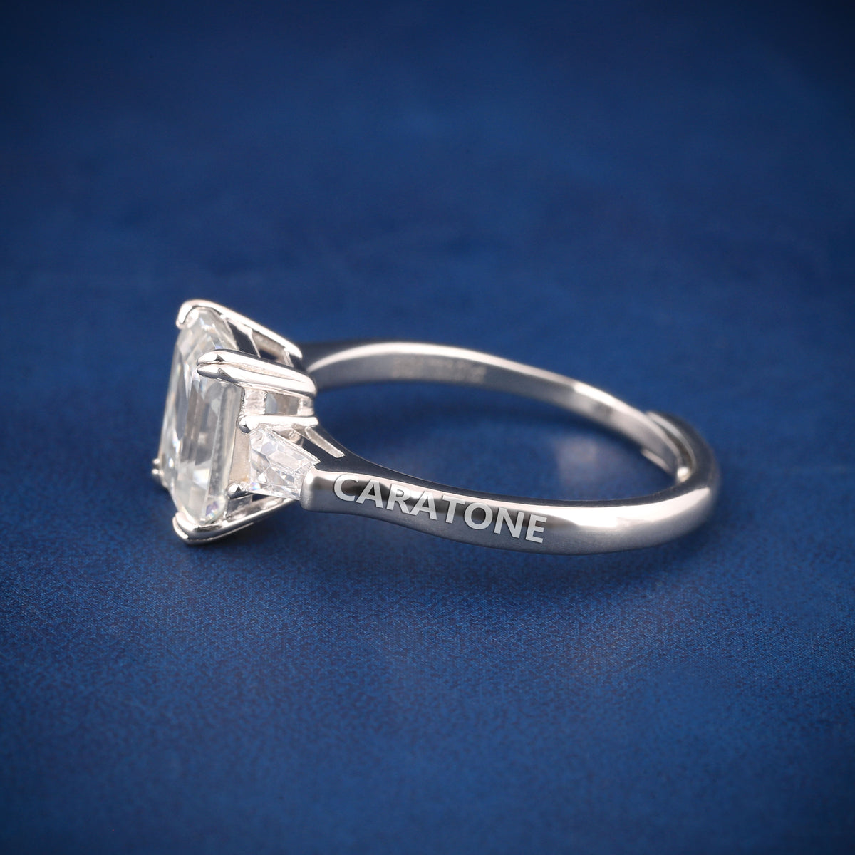 Premium Luxury Emerald Cut Solitaire Ring With Brilliant White Center Stone, Elegant Trapezoid Side Stones, Classic Silver Tone Band And Exclusive Designer Engagement Jewelry For Women