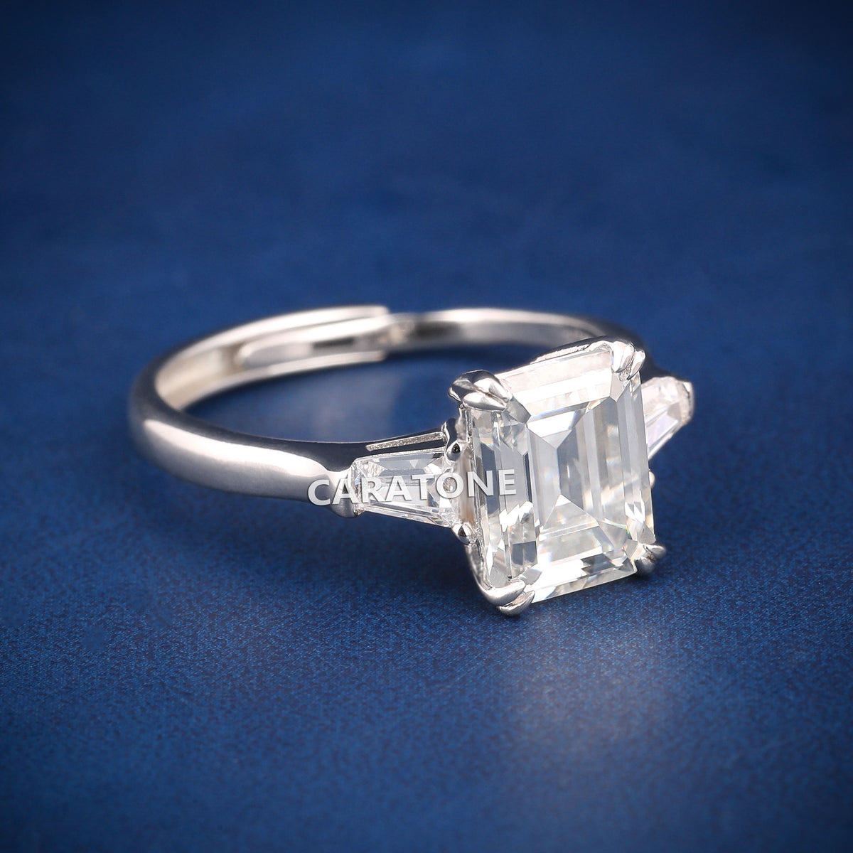 Premium Luxury Emerald Cut Solitaire Ring With Brilliant White Center Stone, Elegant Trapezoid Side Stones, Classic Silver Tone Band And Exclusive Designer Engagement Jewelry For Women